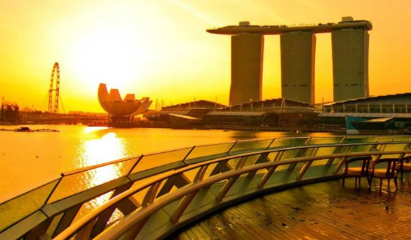 Imagem deslumbrante de Singapura ao pôr do sol, com vista para Marina Bay Sands, a roda gigante e edifícios modernos refletindo na água, criando uma paisagem urbana impressionante.