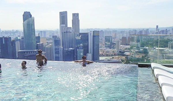 Pessoas relaxando na piscina no topo do Hotel Marina Bay com vista para a cidade de Singapura, com arranha-céus ao fundo.