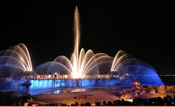 Espetáculo de fontes luminosas no lago à noite, com jatos de água iluminados em cores azul e roxo, criando um cenário vibrante e deslumbrante. Singapura e os pontos turísticos.
