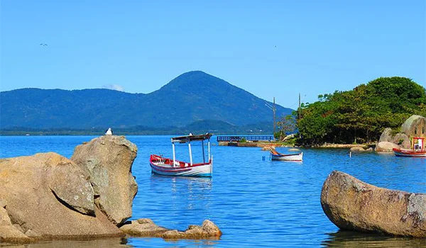 Bonita foto do mar de Santa Catarina com barcos pequenos entre montanhas e pedras.