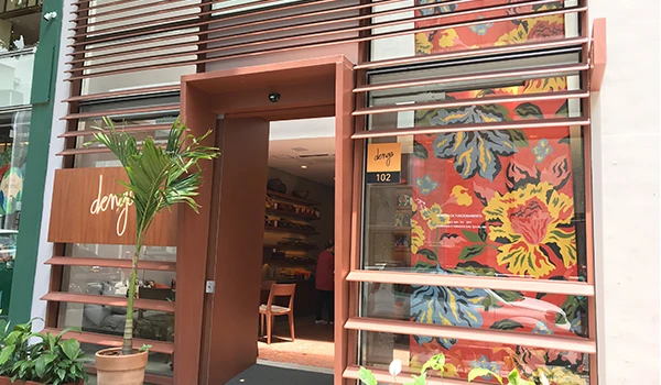 Fachada de uma loja de chocolates com design moderno e colorido, com entrada em madeira e decoração com plantas naturais, promovendo um ambiente acolhedor e elegante.