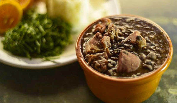 Prato de feijoada tradicional brasileira servido em uma tigela de barro, acompanhado de arroz, farofa e couve, ideal para refeições completas.