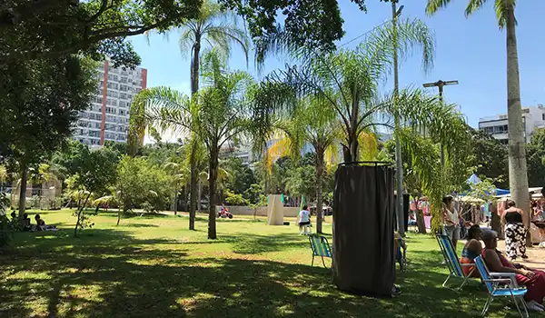 Parque urbano com várias palmeiras, pessoas relaxando em bancos e sombra na cidade, ambiente tranquilo e arborizado ideal para lazer ao ar livre.