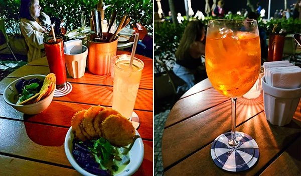 Imagem de um ambiente ao ar livre com comida e drinks, incluindo uma porção de fried chicken, salada e bebidas refrescantes em um cenário de restaurante ou catering. Viagens para Ipanema.