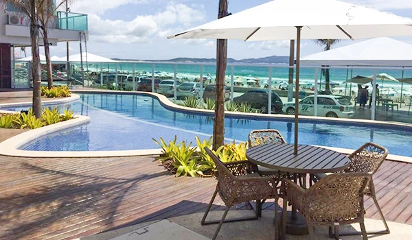 Área de lazer com piscina e vista para o mar, cadeiras de fibra, guarda-sóis e ambiente externo em um resort à beira-mar. Lua de Mel em Cabo Frio.