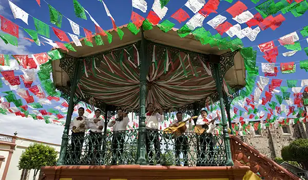 Celebração tradicional com músicos tocando em um palco ao ar livre decorado com bandeiras coloridas para festas tradicionais brasileiras. Viagem ao México.