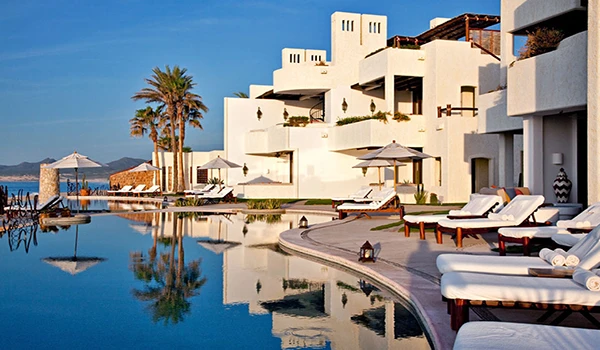 Vista de um resort de luxo com piscina de borda infinita, espreguiçadeiras, palmeiras e vista para o mar, ideal para quem busca férias de alto padrão.