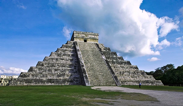 Pirâmide de Chichen Itza, antiga construção maia localizada na civilização maia, destaca-se na paisagem com céu azul e nuvens brancas ao fundo. Viagem ao México.