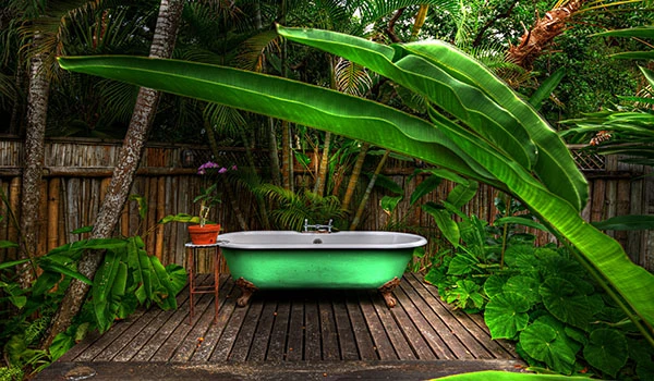 Banheira antiga de ferro fundido branca ao ar livre, rodeada por plantas verdes exuberantes e um jardim tropical, criando um ambiente relaxante.