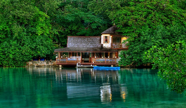 Casa rústica localizada à beira de um rio cercada por árvores verdes em um cenário natural tranquilo. Vista exótica e ideal para relaxar na natureza.