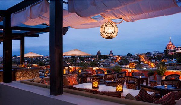 Vista panorâmica de um rooftop de restaurante com iluminação aconchegante à noite, decorado com lampiões.