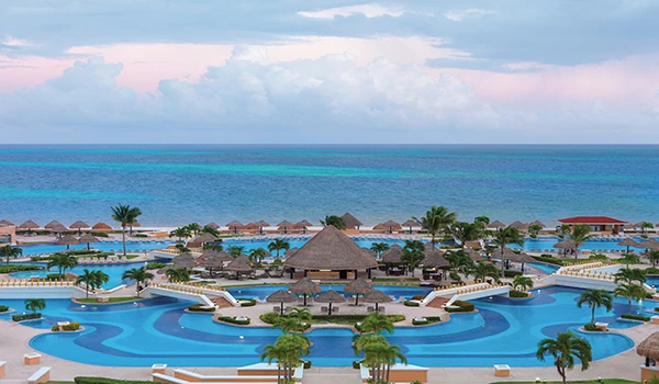 Imagem de um resort de luxo com piscinas, palmeiras, espreguiçadeiras e vista para o mar na praia, perfeito para férias na praia.