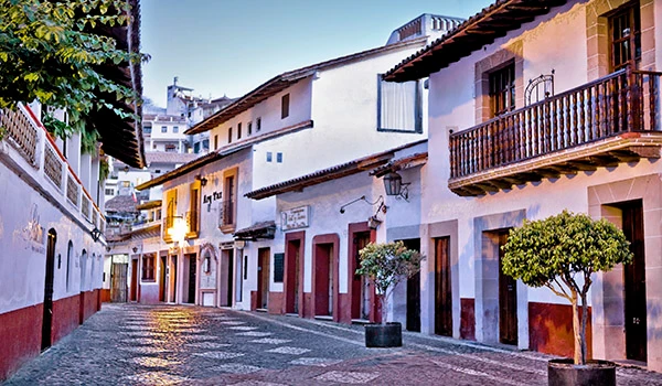 Cenário de rua colonial no centro histórico, com casas tradicionais, calçada de pedra, árvores verdes e iluminação suave durante o dia, ideal para turismo e cultura. Viagem ao México.