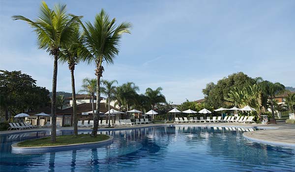 Linda piscina em um resort tropical, cercada por palmeiras e espreguiçadeiras, perfeita para relaxar e aproveitar o sol.