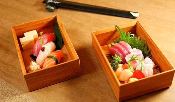 Imagem de sashimis variados em caixotes de madeira, acompanhados de hortelã, limão e outros acompanhamentos, ideal para pratos de comida japonesa.