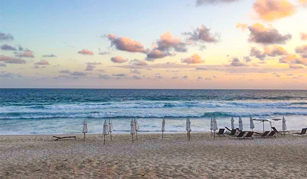 Praia ao entardecer guarda-sóis cadeiras de praia ao longo da areia, mar calmo e céu com nuvens coloridas, ideal para relaxar, dicas sobre o que fazer na Barra da Tijuca.