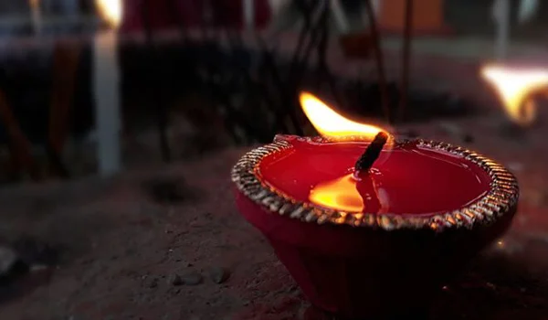 Uma lamparina de barro decorativa, com óleo e pavio acesos, emitindo uma chama brilhante em um ambiente escuro e acolhedor.