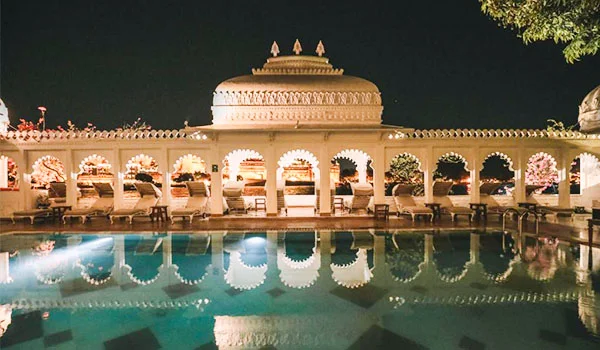 Vista noturna do Taj Lake Palace, em Udaipur, com uma fachada palaciana iluminada e ornamentada refletida na piscina.