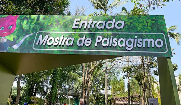 Foto da entrada com painel entre árvores da Entrada da Mostra de Paisagismo.