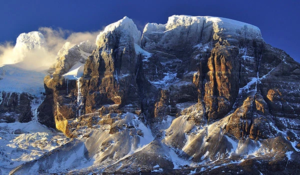 Montanhas cobertas de neve sob um céu azul, destacando as formações rochosas e o cenário de inverno na natureza selvagem.