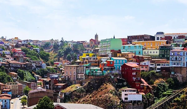 Vibrante vista aérea de um bairro colorido na cidade,mostrar casas em diferentes tons e morros, refletindo a diversidade urbana e cultural, com céu claro ao fundo. Lua de Mel no Chile.