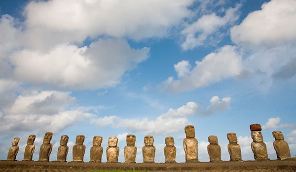 Imagem das famosas Moais na Ilha de Páscoa, com céu azul e nuvens brancas ao fundo, destacando a cultura e história local.