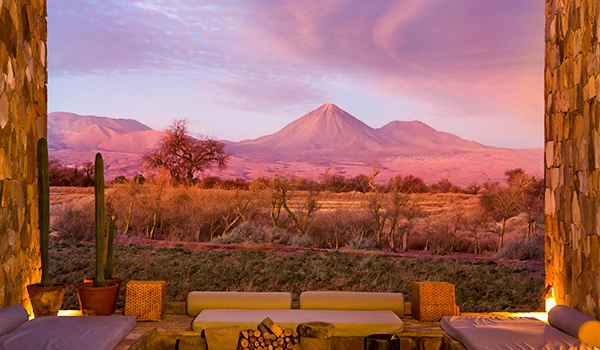 Paisagem desértica em uma tarde com montagem de montanhas ao fundo, vista de uma varanda com móveis de madeira e decorações rústicas. Lua de Mel no Chile.