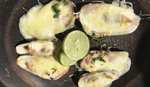 Ostras gratinadas com queijo, acompanhadas de fatias de limão, em uma tábua de pedra, destacando uma deliciosa preparação de frutos do mar.