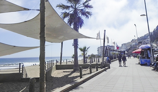 Passeio na orla da praia com calçadão, palmeiras, quiosques e vista do mar em um dia ensolarado na orla de uma cidade costeira. Chile pontos turísticos.