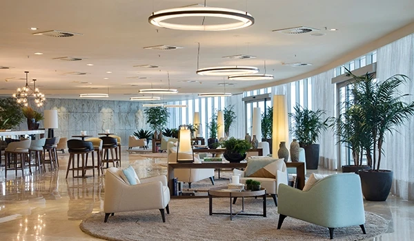 Imagem de um elegante salão de eventos com poltronas, mesas de centro, plantas decorativas e iluminação moderna, ideal para reuniões e eventos sociais.