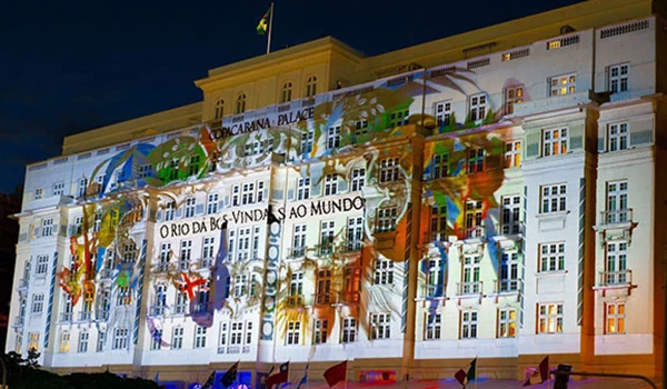 Edifício histórico iluminado com uma projeção colorida durante uma celebração ou evento especial, exibindo uma mensagem de boas-vindas ao mundo impecável.