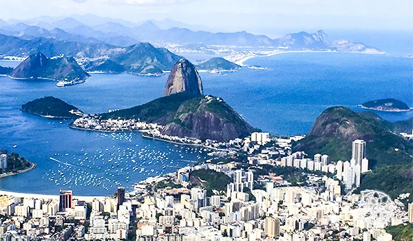 Vista panorâmica do Rio de Janeiro com praias, montanhas e o icônico Pão de Açúcar sob céu nublado, destacando a beleza natural e urbana da cidade.