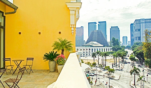 Vista de uma cidade moderna e vibrante vista de um terraço com plantas, com edifícios altos e arquitetura contemporânea ao fundo.