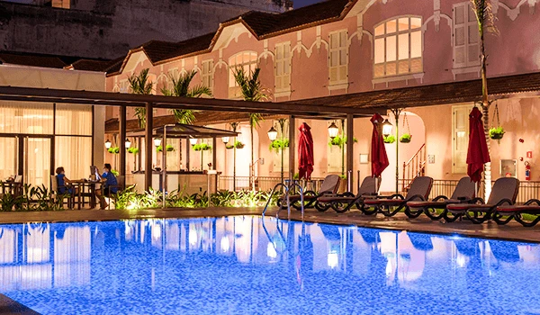 Piscina iluminada à noite em um hotel com espreguiçadeiras ejada de plantas, criando um ambiente relaxante e aconchegante para os hóspedes.