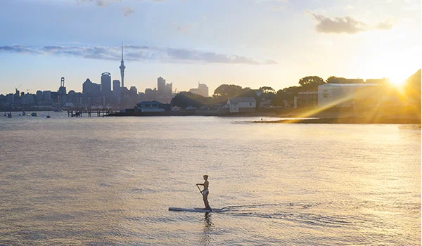 Foto de uma mulher em um stand up no mar ao pôr do sol em Auckland na Lua de Mel na Nova Zelândia.