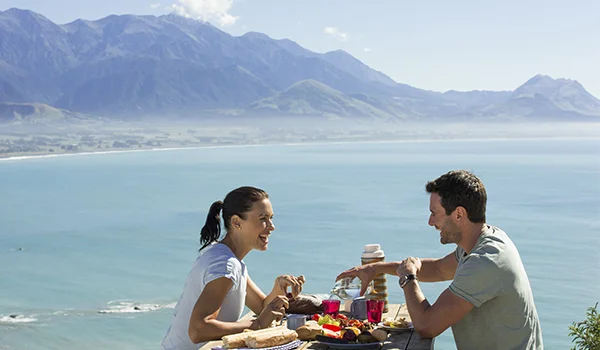 foto de um casal almoçando em Kaikoura Canterbury, com vista deslumbrante da água e das montanhas.