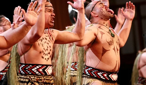 Foto de um grupo de dançarinos da Cultura Maori, com corpos tatuadas e roupas típicas.