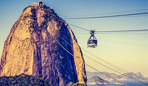 Bondinho na praia do Rio de Janeiro com vista para a rocha do Pão de Açúcar ao entardecer, promovendo turismo e lazer na cidade.