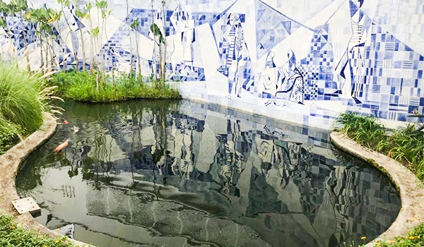 Piscina urbana decorada com azulejos azuis e branco, rodeada de plantas verdes em um espaço ao ar livre, ideal para lazer e relaxamento.