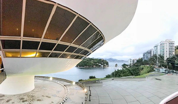 Imagem do Museu de Niterói, destacando sua arquitetura futurista e vista para a Baía de Guanabara, com prédios modernos ao redor.