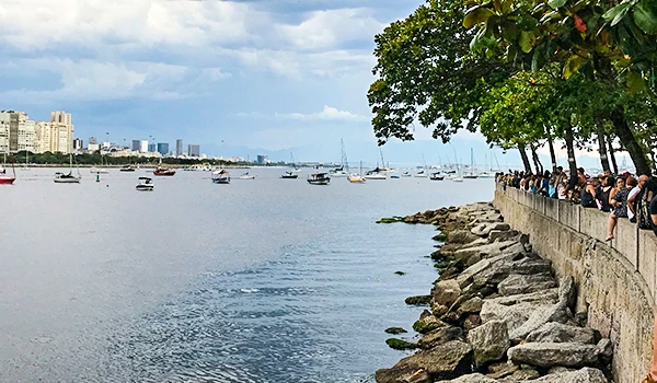 Caminhada na orla com vista de prédiosm árvores ao lado e pessoas aproveitando o dia ao ar livre.