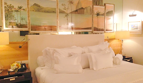 Quarto de hotel aconchegante com cama bem arrumada, quadros de paisagens ao fundo e iluminação confortável, ideal para relaxar durante viagens.