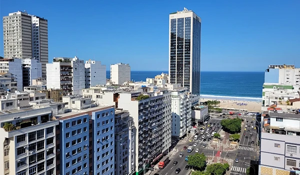 Imagem de arranha-céus modernos na cidade litorânea do Rio de Janeiro com vista para o mar ao fundo, destacando a infraestrutura urbana e o clima ensolarado.