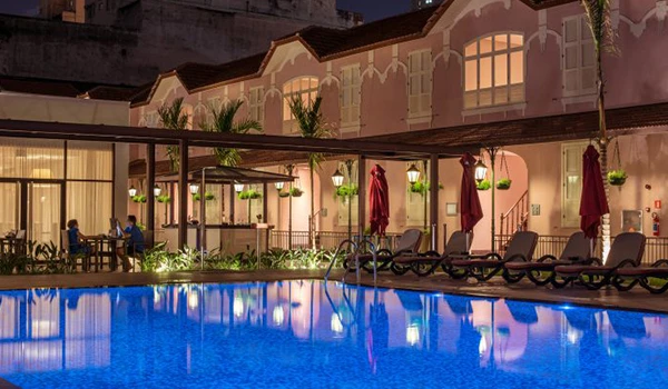 Piscina de hotel à noite com espreguiçadeiras e iluminação aconchegante, ideal para relaxar e aproveitar momentos de lazer em um ambiente confortável.