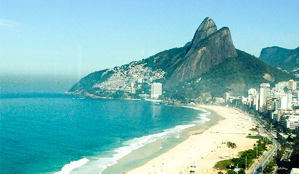 Praia de Ipanema no Rio de Janeiro com seu mar azul, areia dourada e o famoso morro Dois Irmãos ao fundo, cenário icônico da cidade.