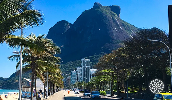 Vista de um restaurante em um andar alto com mesas e cadeiras, com panorama para um rio tranquilo, áreas verdes e edifícios ao fundo, sob céu parcialmente nublado.