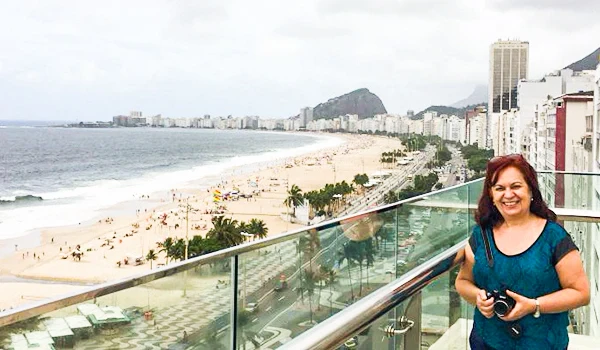 Deusa Rodrigues em varanda com vista de uma grande praia e cidade ao fundo, durante o dia, na orla de uma cidade costeira famosa.