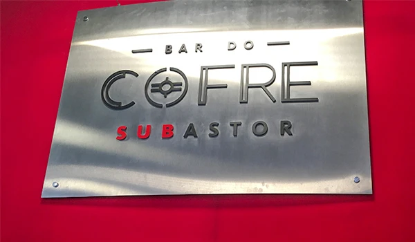 Fachada do Bar do Cofre Subastor, ambiente moderno com letreiro de metal e fundo vermelho.