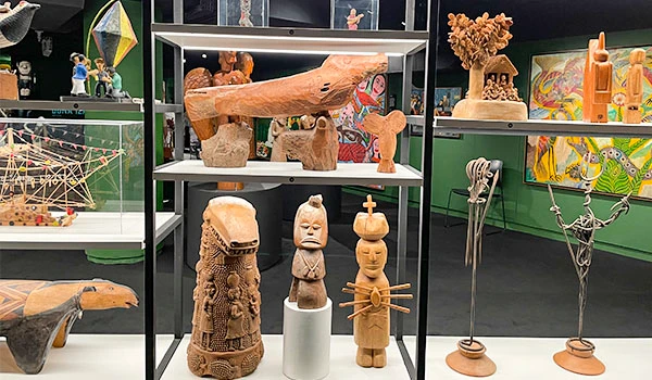 Exposição de esculturas e artesanato indígena em uma vitrine de museu, com destaque para peças de madeira, cerâmica e arte tribal.