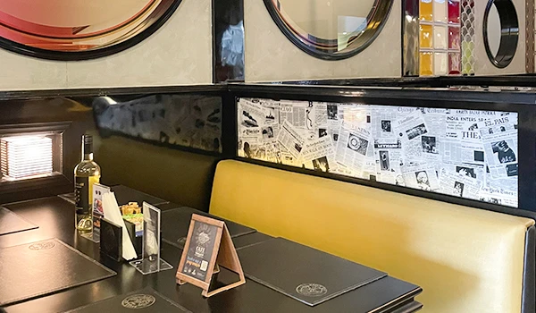 Interior de um restaurante moderno com decoração em estilo newsprint na parede, bancos amarelos e mesas bem arrumadas com detalhes elegantes.